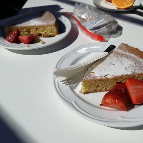 Teller mit einem Stück Biskuitkuchen und frischen Erdbeeren auf einem weißen Tisch.