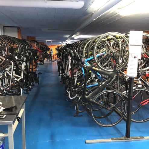 Innenansicht eines Fahrradlagers mit mehreren Fahrrädern, die an der Wand hängen, und einem Tisch mit mehreren Gegenständen.