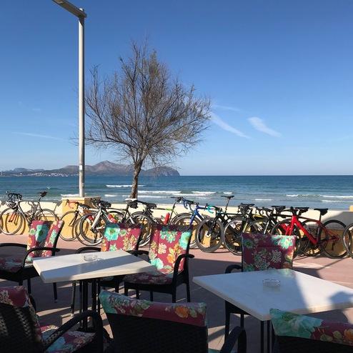 Blick auf das Meer mit Fahrrädern und blühenden Stühlen an einem Tisch in einem Strandrestaurant.