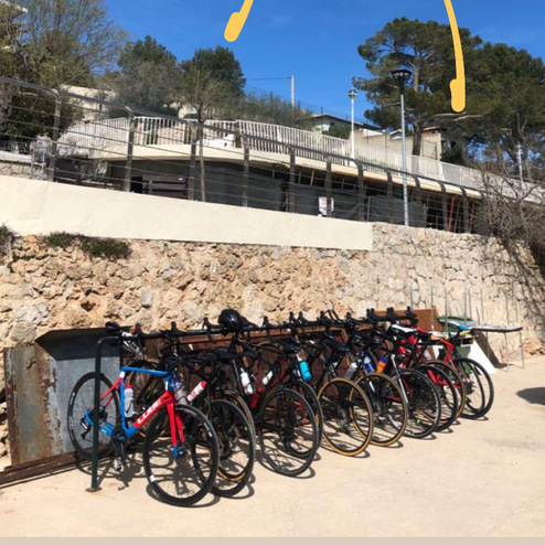 Acht Fahrräder stehen an einem Parkplatz mit blauen Himmel und Sonnenschein im Hintergrund.