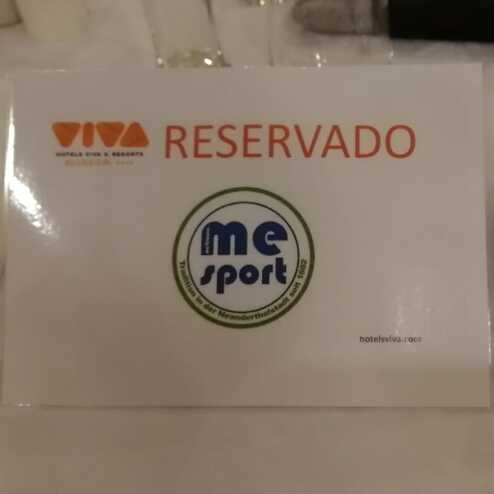 Tischreservierungsschild mit dem Aufdruck „RESERVADO“ und einem Logo von „me sport“ neben einem leeren Teller.