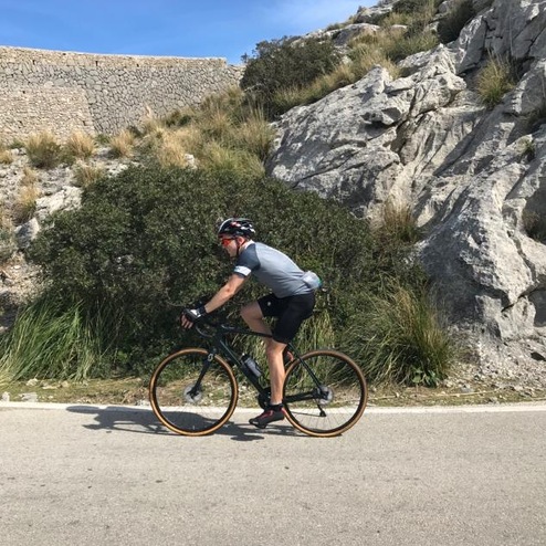 Radfahrer in sportlicher Kleidung fährt auf einer kurvigen Straße entlang einer felsigen Landschaft.