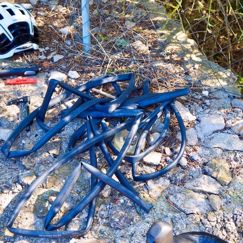 Schwarze Fahrradschläuche und Werkzeug liegen auf einer steinernen Fläche neben einem Fahrradhelm.