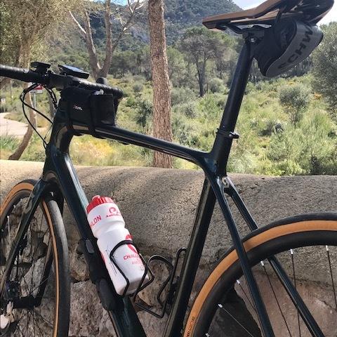 Nahaufnahme eines Rennrads mit Trinkflasche, im Hintergrund ein Hügel mit einer Burg und Bäumen.