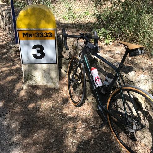 Fahrrad steht neben einem gelben Wegweiser mit der Aufschrift "Ma-3333" und der Zahl "3" auf einem ruhigen Waldweg.