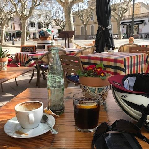 Tisch mit einer Kaffeetasse, einem Glas Wasser, einem Keks und einer Pflanze in einem Freiluftcafé.