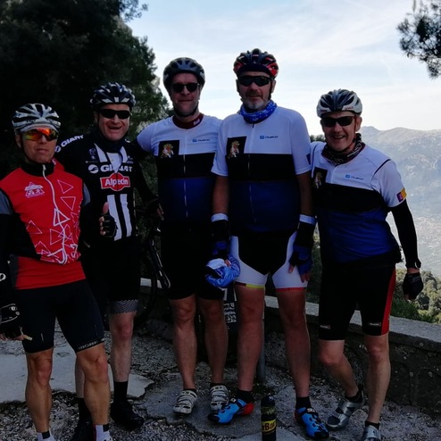Gruppe von fünf Radfahrern in Sportbekleidung posiert an einem Aussichtspunkt mit Berglandschaft im Hintergrund.