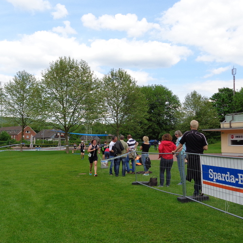Zuschauer stehen an einem Zaun, während Teilnehmer einen Wettkampf auf einer grünen Wiese absolvieren.