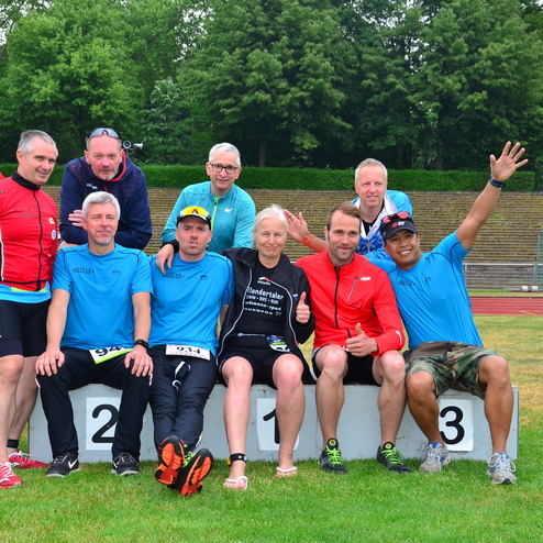Gruppe von Sportlern auf dem Siegerpodest, lächelnd, nach einem Wettkampf auf einem Stadionrasen.