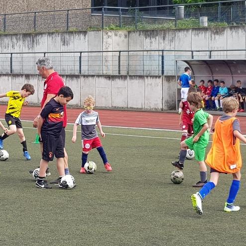 Eine Gruppe von Kindern trainiert Fußball auf einem Kunstrasenplatz unter Anleitung eines Trainers.