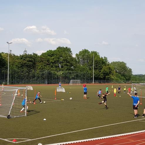 Kinder trainieren Fußball auf einem Kunstrasenplatz mit mehreren kleinen Toren und Trainingshindernissen.