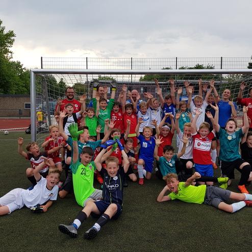 Gruppenshot von Kindern in Fußballtrikots, die vor einem Tor freudig posieren und die Hände in die Luft werfen.