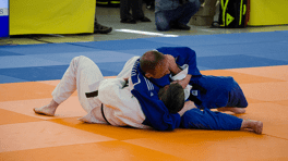 Zwei Judokas im Wettkampf auf einer blauen und orangefarbenen Matte, einer in weißem und der andere in blauem Anzug.
