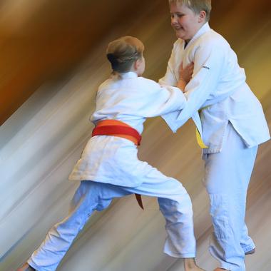 Zwei Kinder im Judogi kämpfen auf einem verschwommenen Hintergrund, eines hat einen roten, das andere einen gelben Gürtel.