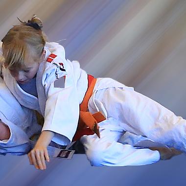 Zwei Kinder im Judoanzug kämpfen lächelnd in der Luft, umgeben von einem unscharfen, farbigen Hintergrund.