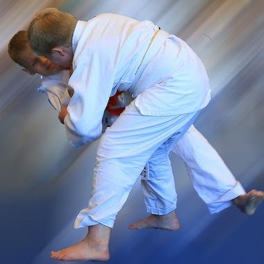 Zwei Kinder in weißen Judoanzügen führen einen Wurf im Judo auf einer blauen Matte aus.
