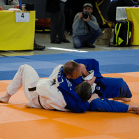 Zwei Judokas im Wettkampf auf einer blauen und orangefarbenen Matte, einer in weißem und der andere in blauem Anzug.