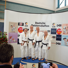 Vier Judokas in weißen Judogis mit Medaillen stehen lächelnd vor einem Banner mit der Aufschrift „Deutsche Meisterschaften“.