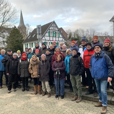 Gruppe von 30 Personen in warmen Winterkleidern steht auf einer Treppe vor Fachwerkhäusern und einem Kirchturm.