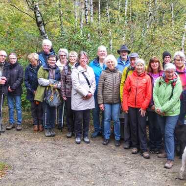 Gruppe von 25 Personen in Outdoor-Kleidung, umgeben von Bäumen, einige Hunde sind ebenfalls dabei.