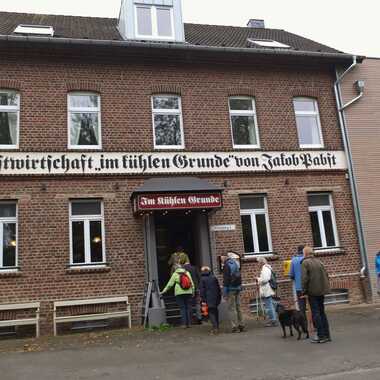 Eingang der Gastwirtschaft „Im kühlen Grunde“ mit Warteschlange vor der Tür und mehreren Besuchern.