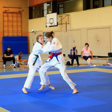 Zwei Judokas im Wettkampf auf einer blauen Matte, umgeben von Zuschauern in einem Sportzentrum.