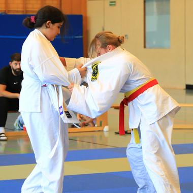 Zwei Kinder in Judoanzügen üben einen Griff auf einer blauen Judomatte während eines Trainings.
