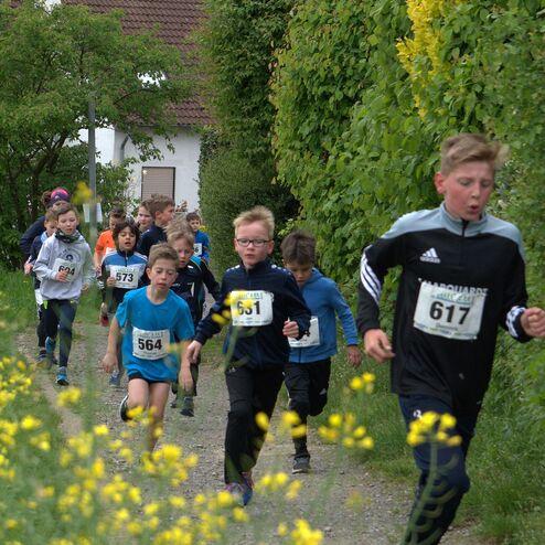 Gruppe von Kindern in Sportkleidung läuft einen Waldweg entlang, umgeben von Gelbblühenden Pflanzen.