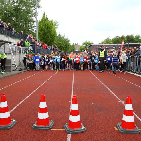 Gruppierung von Kindern an der Startlinie eines Wettlaufs, umgeben von Zuschauern und Sicherheitskonen auf einer Laufbahn.