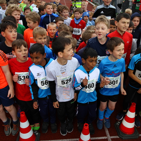 Gruppe von Jungen in Sportkleidung mit Startnummern, versammelt vor einem Wettlauf, einige posieren und lachen.
