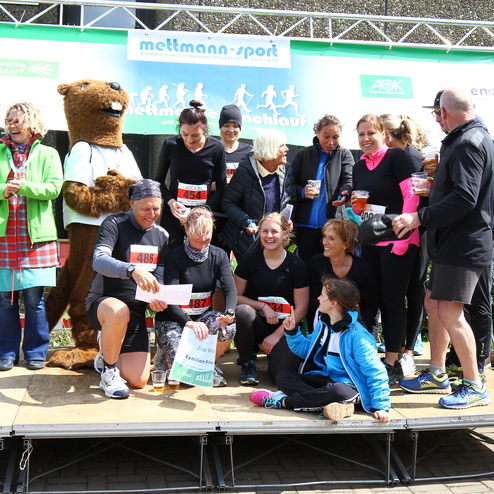 Gruppe von Läufern auf der Bühne nach einem Wettlauf, umgeben von Zuschauern und einem Maskottchen.