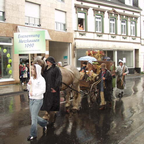 Pferd zieht einen Wagen mit Blumen, während Menschen in Regenkleidung bei einer Feier auf der nassen Straße laufen.