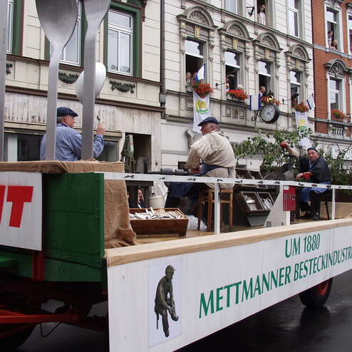 Fahrt auf einem Festwagen mit großen Besteckteilen und mehreren Personen in historischen Kostümen.