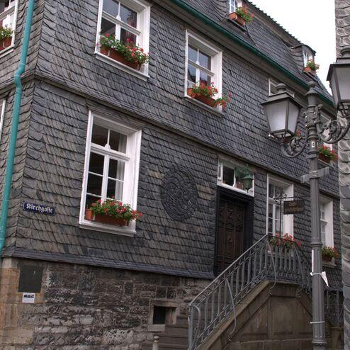 Fassade eines Hauses mit grauen Schieferplatten, Blumentöpfen und einer Laterne an der Außentreppe zur Eingangstür.