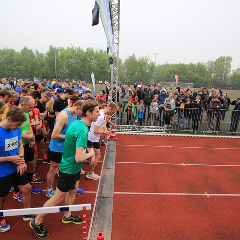 Gruppierung von Läufern am Start eines Rennens, umgeben von Zuschauern auf einer Sportanlage.