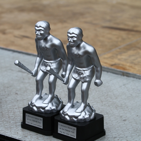 Vier silberne Pokale in Form von Menschen mit Schlägern stehen auf einer Tischoberfläche.