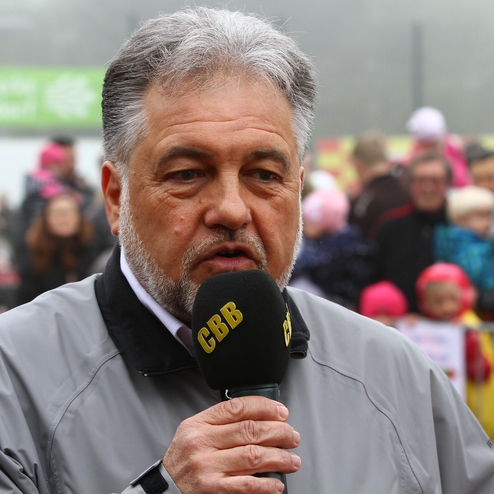 Mann mit grauen Haaren spricht in ein Mikrofon vor einer Menschenmenge bei einem Event im Freien.
