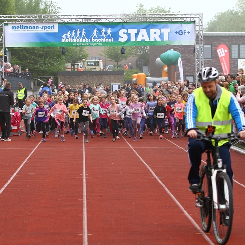Start eines Kinderlaufs mit vielen jungen Teilnehmern, die auf der roten Laufbahn in Richtung Ziel laufen.