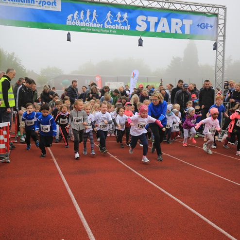 Startschuss für ein Kinderlauf-Event: zahlreiche Kinder sprinten auf einer roten Laufbahn, umgeben von Zuschauern.