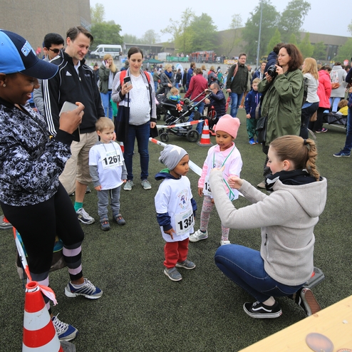 Gruppenevent mit Kindern in Laufshirts, Medaillenübergabe und Zuschauern auf einem Sportplatz bei nebligem Wetter.