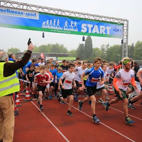 Start eines Schülerlaufes mit zahlreichen Teilnehmern, die auf einer Tartanbahn loslaufen. Ein Schiedsrichter gibt das Signal.
