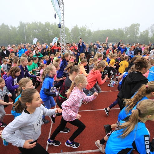 Gruppstart von Mädchen in Sportkleidung bei einem Laufereignis auf einem roten Sportplatz, umgeben von Zuschauern.
