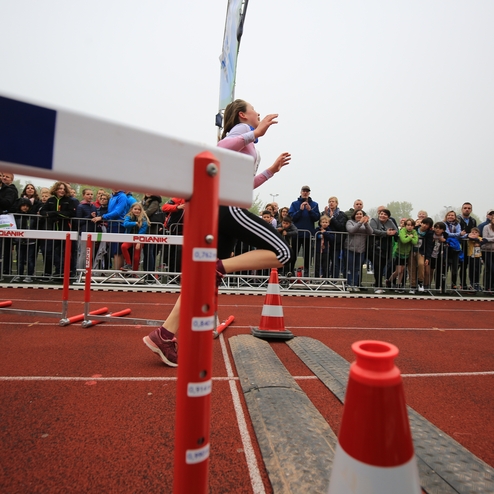 Eine Athletin überquert eine Hürde auf der Laufbahn, umgeben von jubelnden Zuschauern.