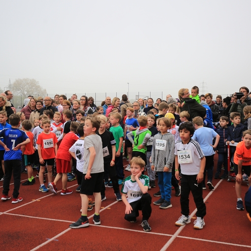 Gruppierung von Kindern in Sportkleidung, die auf dem Laufbahnstartbereich vor Zuschauern warten.