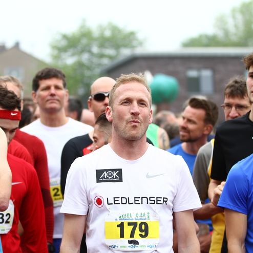 Gruppierung von Läufern vor dem Start eines Wettlaufs, mit verschiedenen Trikots und Startnummern sichtbar.