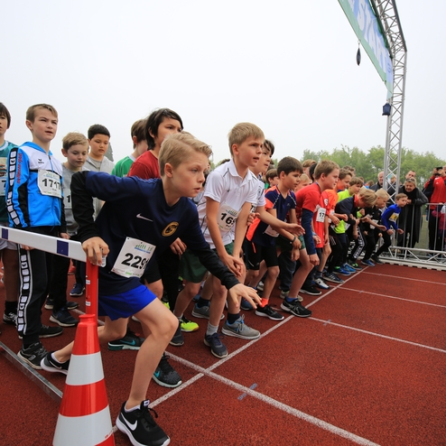 Startgruppe von Kindern an einer Laufveranstaltung, bereit zum Wettlauf auf einer roten Tartanbahn.