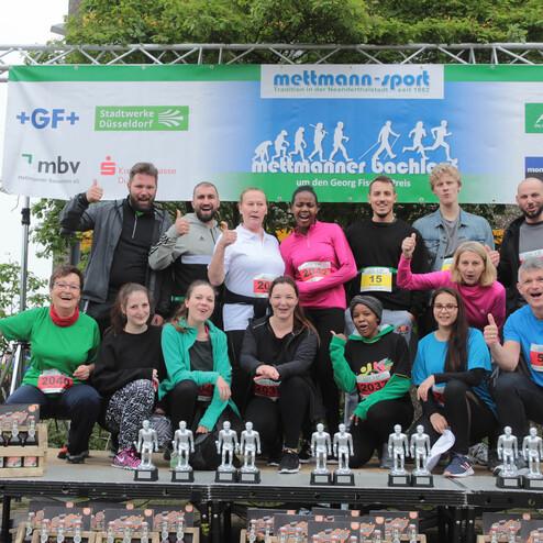 Gruppe von Läufern posiert auf einer Bühne mit Pokalen, während sie an einem Wettlauf in Mettmann teilnehmen.