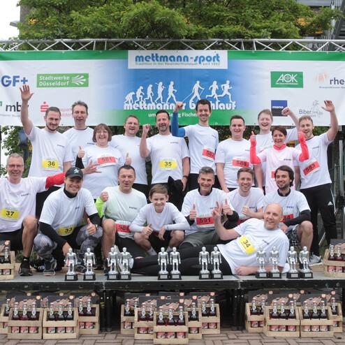 Gruppenfoto von Teilnehmern des Mettmanner Stadtlaufs, in weißen T-Shirts, umgeben von Pokalen und Medaillen.