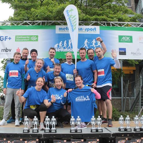 Gruppe von sportlich gekleideten Personen posiert fröhlich auf einer Bühne mit Pokalen bei einer Sportveranstaltung.