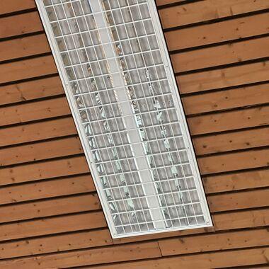 Decke mit Holzpaneelen und einer rechteckigen, gitterförmigen Deckenleuchte in der Mitte.